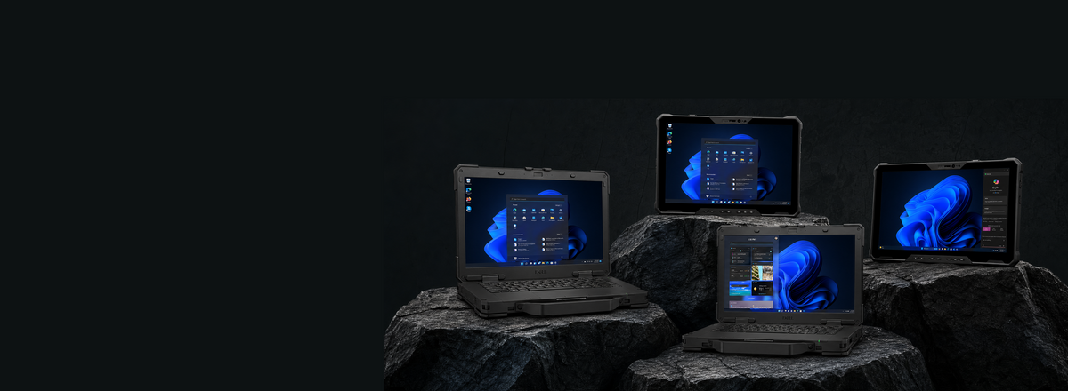 Four rugged black laptops and a tablet displaying a blue Windows desktop setup, arranged on dark rocks against a black background.