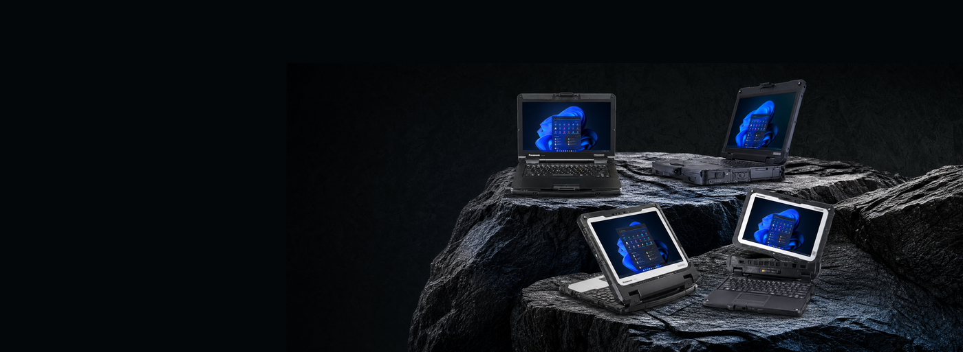 Four silver laptops with glowing blue screens are arranged on a dark rocky surface against a black background.